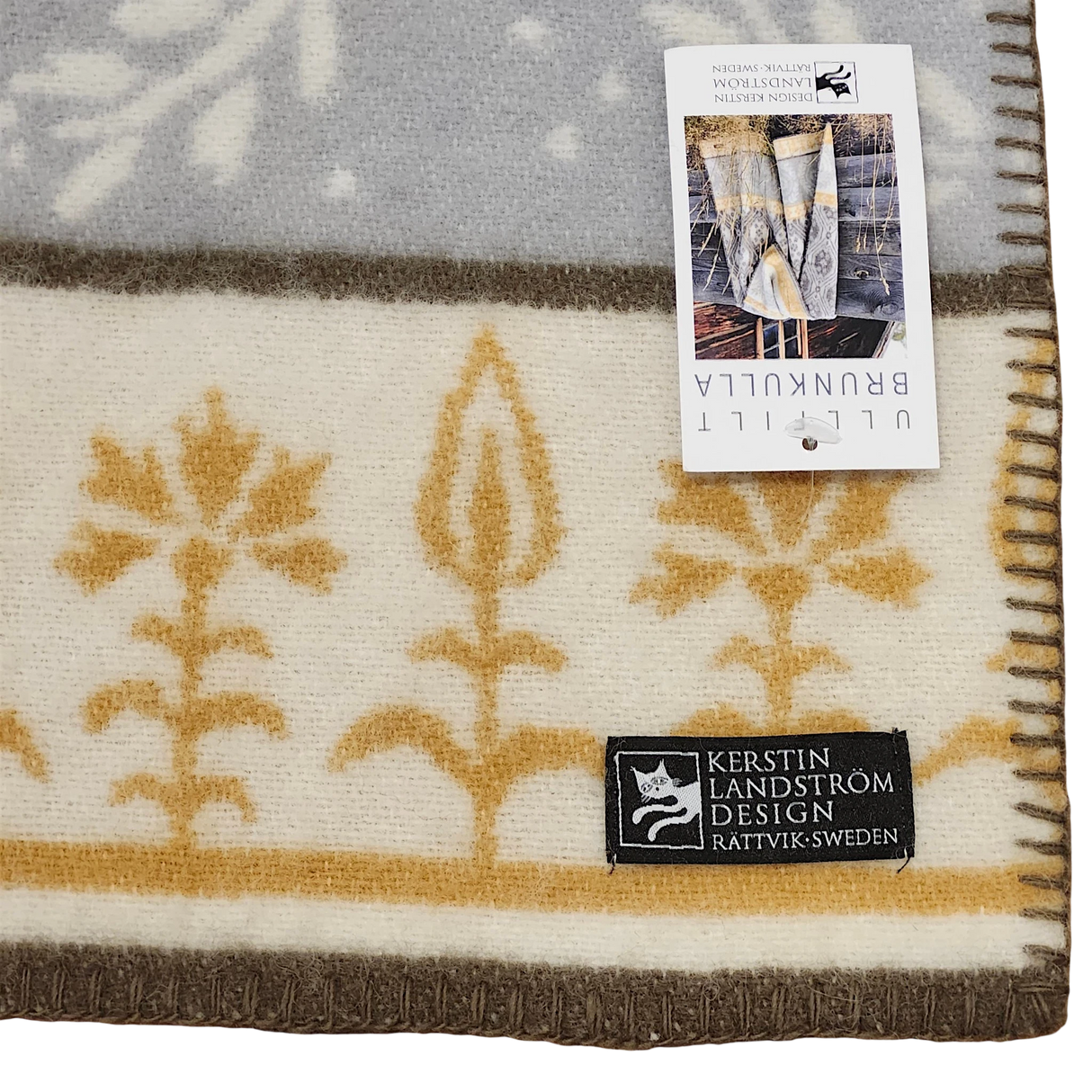 Swedish wool blanket with beige and gold floral pattern, shown with two tags; one displays product info, the other reads Kerstin Landström Design, Rättvik, Sweden.