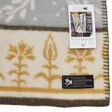 Swedish wool blanket with beige and gold floral pattern, shown with two tags; one displays product info, the other reads Kerstin Landström Design, Rättvik, Sweden.