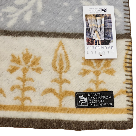 Swedish wool blanket with beige and gold floral pattern, shown with two tags; one displays product info, the other reads Kerstin Landström Design, Rättvik, Sweden.