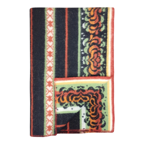 Bunad blanket with orange, black, green, and cream stripes, floral patterns, contrasting borders, and a turned-up corner showing the underside.
