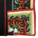Folded Bunad blanket with red, orange, and green floral patterns, yellow and white stripes, and red zigzag stitching along the edge.