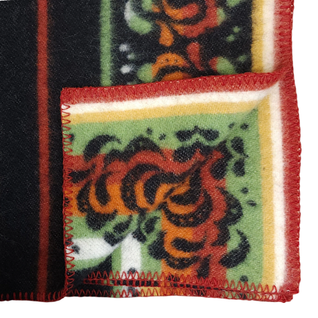 Folded Bunad blanket with red, orange, and green floral patterns, yellow and white stripes, and red zigzag stitching along the edge.