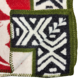 Close-up of a blanket corner showing green stitched edging, black and white geometric patterns, and red sections on soft lambswool fabric.