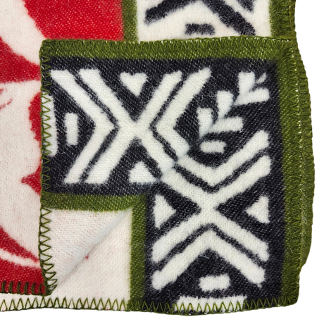 Close-up of a blanket corner showing green stitched edging, black and white geometric patterns, and red sections on soft lambswool fabric.