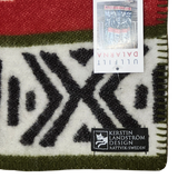 Lambswool blanket featuring black geometric patterns, red and green stripes, Swedish Dala Horses, and two visible tags including one labeled Kerstin Landström Design.