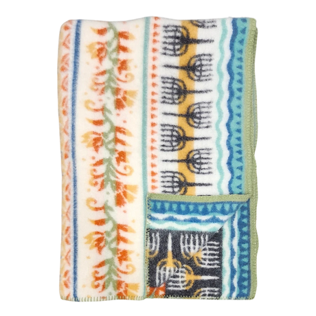 Folded fleece blanket with green trim, orange floral and blue geometric patterns on a cream background, showing Swedish-inspired design.