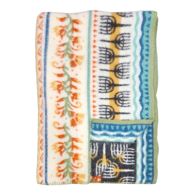 Folded fleece blanket with green trim, orange floral and blue geometric patterns on a cream background, showing Swedish-inspired design.