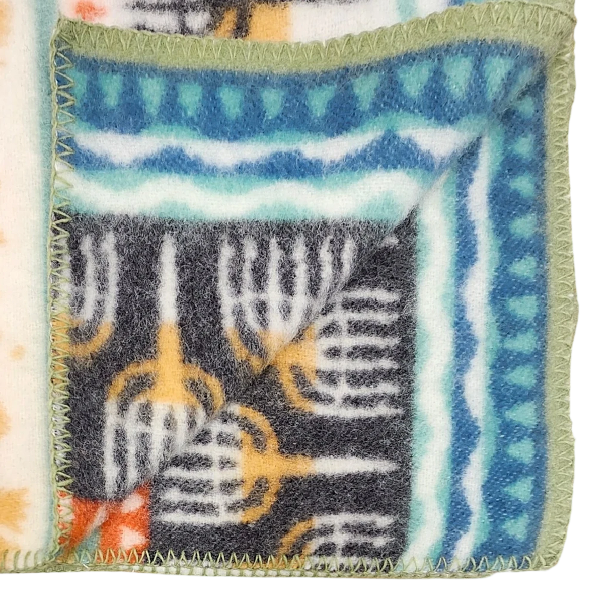 Close-up of a lambswool blanket featuring Swedish geometric patterns in blue, green, orange, and black, with green-stitched edges and one corner folded over.