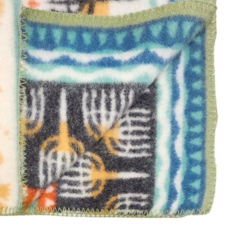 Close-up of a lambswool blanket featuring Swedish geometric patterns in blue, green, orange, and black, with green-stitched edges and one corner folded over.