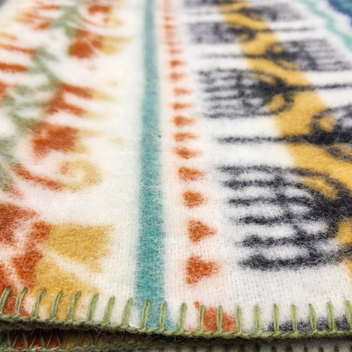 Close-up of a colorful lambswool blanket with Swedish-inspired patterns and green edge stitching, showing detailed texture.