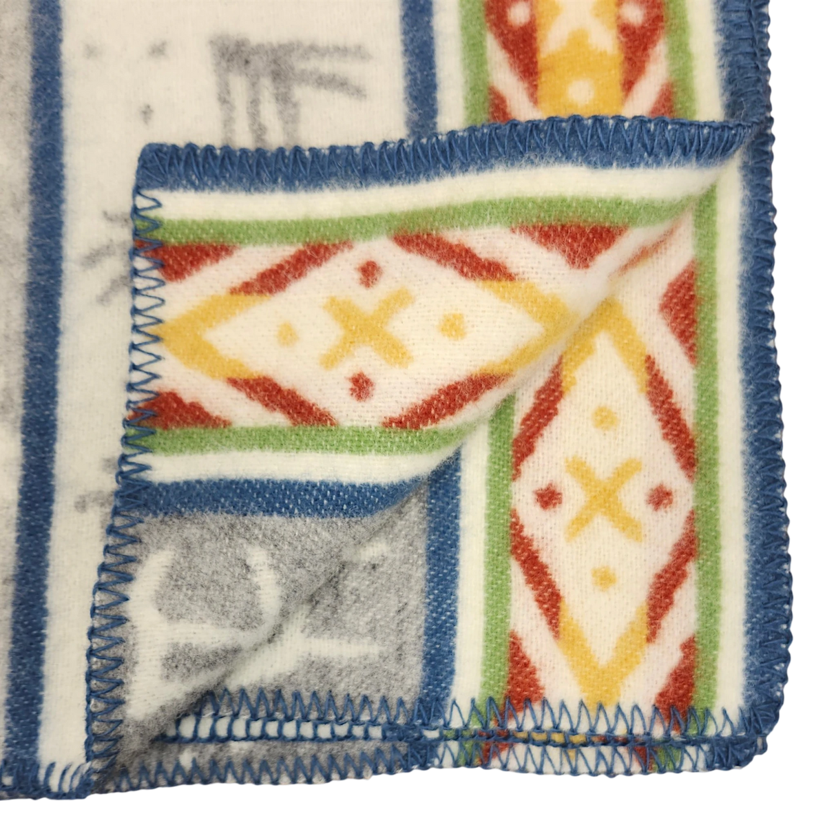 Close-up of a Sámi-inspired wool blanket corner, folded to show both sides, featuring geometric patterns and blue edge stitching.