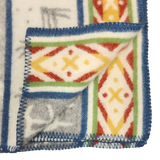 Close-up of a Sámi-inspired wool blanket corner, folded to show both sides, featuring geometric patterns and blue edge stitching.