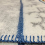 Close-up of a Sámi-inspired wool blanket in white and gray, featuring blue edge stitching and a single blue stripe running down the center.