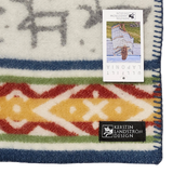 Wool blanket with Sámi-inspired geometric patterns, blue trim, and two labels—one for care instructions and one for Kerstin Landström Design featuring a sheep logo.