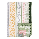 A folded blanket with green, yellow, gray, and pink geometric and floral patterns, plus a small OEKO-TEX certified square displaying matching designs on the edge.