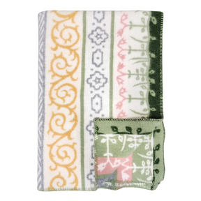 A folded blanket with green, yellow, gray, and pink geometric and floral patterns, plus a small OEKO-TEX certified square displaying matching designs on the edge.