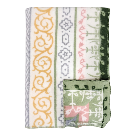 A folded blanket with green, yellow, gray, and pink geometric and floral patterns, plus a small OEKO-TEX certified square displaying matching designs on the edge.