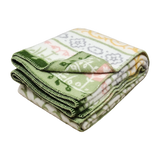 Folded blanket made from Norwegian lambswool with green, yellow, and white floral and geometric patterns on a white background.