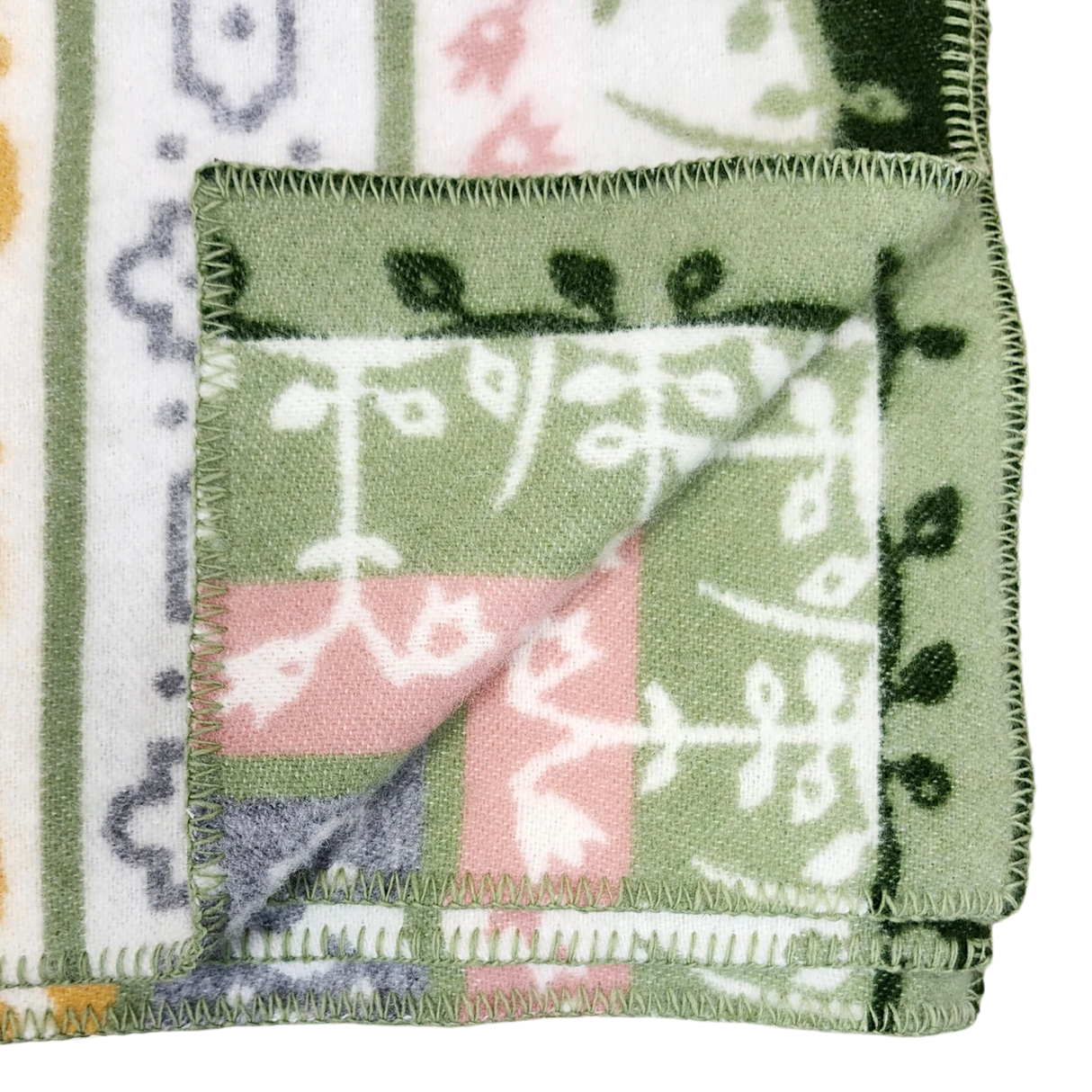Fleece blanket with green, white, pink, and yellow patterns, folded to display both patterned sides and decorative edge stitching.