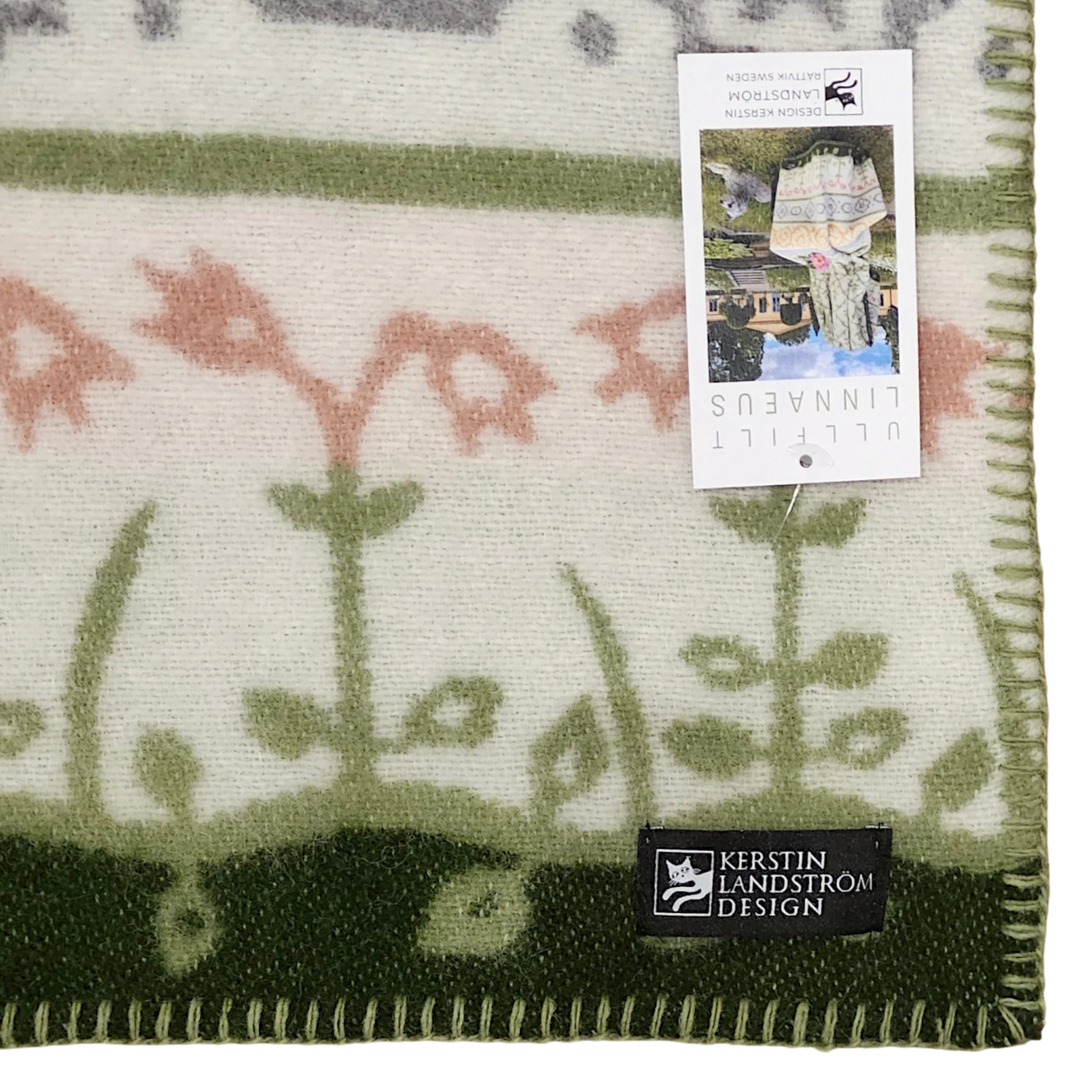 Close-up of a green and cream blanket with floral patterns, visible edge stitching, a Kerstin Landström Design label, product tag, and OEKO-TEX wool tag.