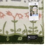Close-up of a green and cream blanket with floral patterns, visible edge stitching, a Kerstin Landström Design label, product tag, and OEKO-TEX wool tag.