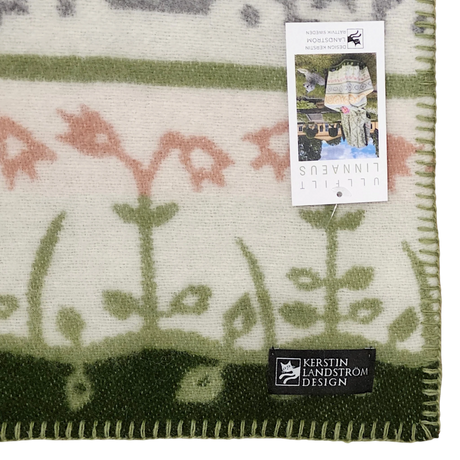 Close-up of a green and cream blanket with floral patterns, visible edge stitching, a Kerstin Landström Design label, product tag, and OEKO-TEX wool tag.