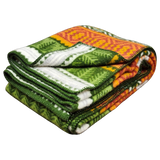 A folded Mora Blanket with green, orange, white, and yellow geometric patterns on a white background, showing Scandinavian design elements.