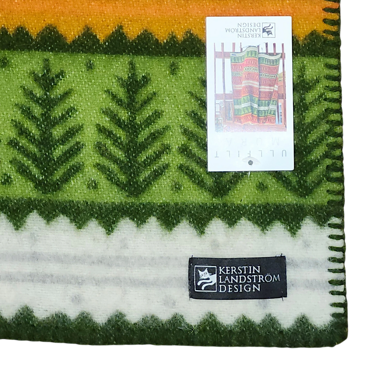 Green, yellow, and white Scandinavian lambswool blanket with tree patterns, a black Kerstin Landström Design label, and a tag displaying the full blanket design.