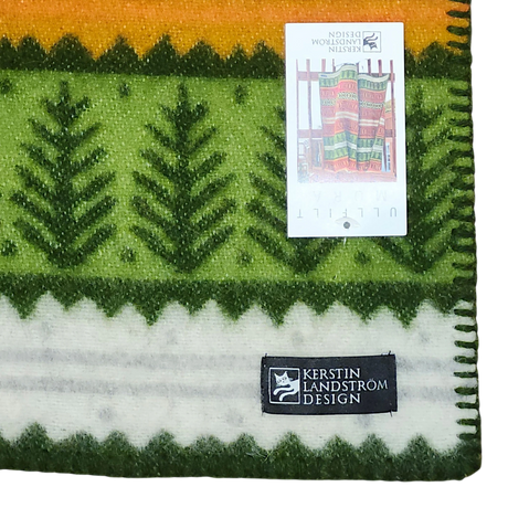 Green, yellow, and white Scandinavian lambswool blanket with tree patterns, a black Kerstin Landström Design label, and a tag displaying the full blanket design.
