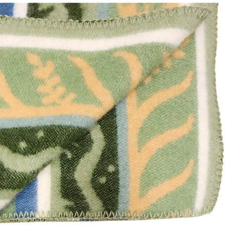 Close-up of a blanket featuring green, beige, and blue Swedish design, with one corner folded to show stitched edges and part of the geometric pattern.
