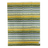 Rectangular Swedish design fabric with horizontal green, blue, white, and yellow stripes, tree and wavy patterns, and a small white tag at the bottom right corner.