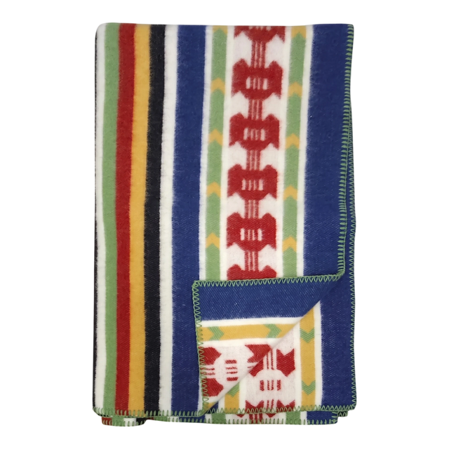 Folded Rättvik wool blanket featuring colorful vertical stripes and geometric patterns; one corner is turned up to show the reverse side.