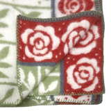Folded blanket featuring red and white rose patterns, green leaves, visible stitched edges, and floral designs on both sides.