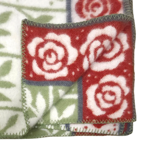 Folded blanket featuring red and white rose patterns, green leaves, visible stitched edges, and floral designs on both sides.