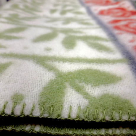 Close-up of a lambswool blanket featuring green and red floral patterns, visible stitching, and elements of Swedish design.