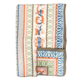 Folded wool blanket with blue, orange, green, and beige animal, floral, and geometric patterns inspired by Swedish folk art, brown trim visible along the edge.