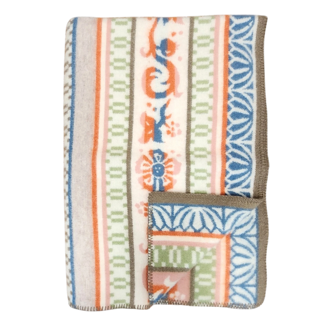 Folded wool blanket with blue, orange, green, and beige animal, floral, and geometric patterns inspired by Swedish folk art, brown trim visible along the edge.