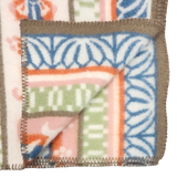 Close-up of a lambswool blanket showing geometric and floral Swedish folk art patterns in blue, green, pink, and orange sections.