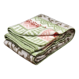 Folded lambswool blanket featuring green, pink, and gray reindeer and snowflake patterns on a white background.