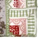 Folded corner of a fleece blanket featuring green, red, white, and beige geometric and floral patterns with zigzag stitching along the edge.