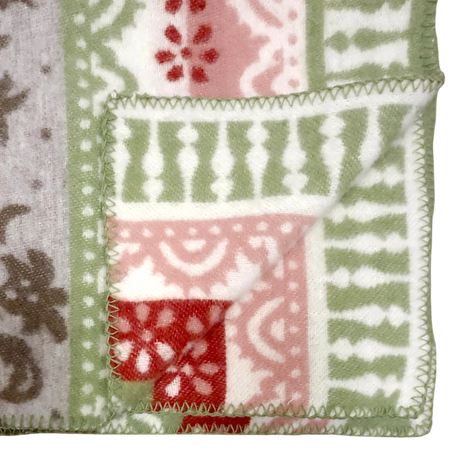 Folded corner of a fleece blanket featuring green, red, white, and beige geometric and floral patterns with zigzag stitching along the edge.