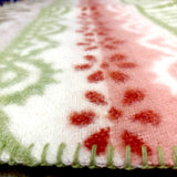 Close-up of a lambswool blanket showing red, white, and green patterns with green edge stitching and visible textured fabric.