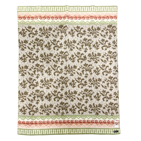 Beige lambswool blanket featuring green and pink borders, a brown leafy pattern in the center, and a small label sewn onto the bottom right corner.