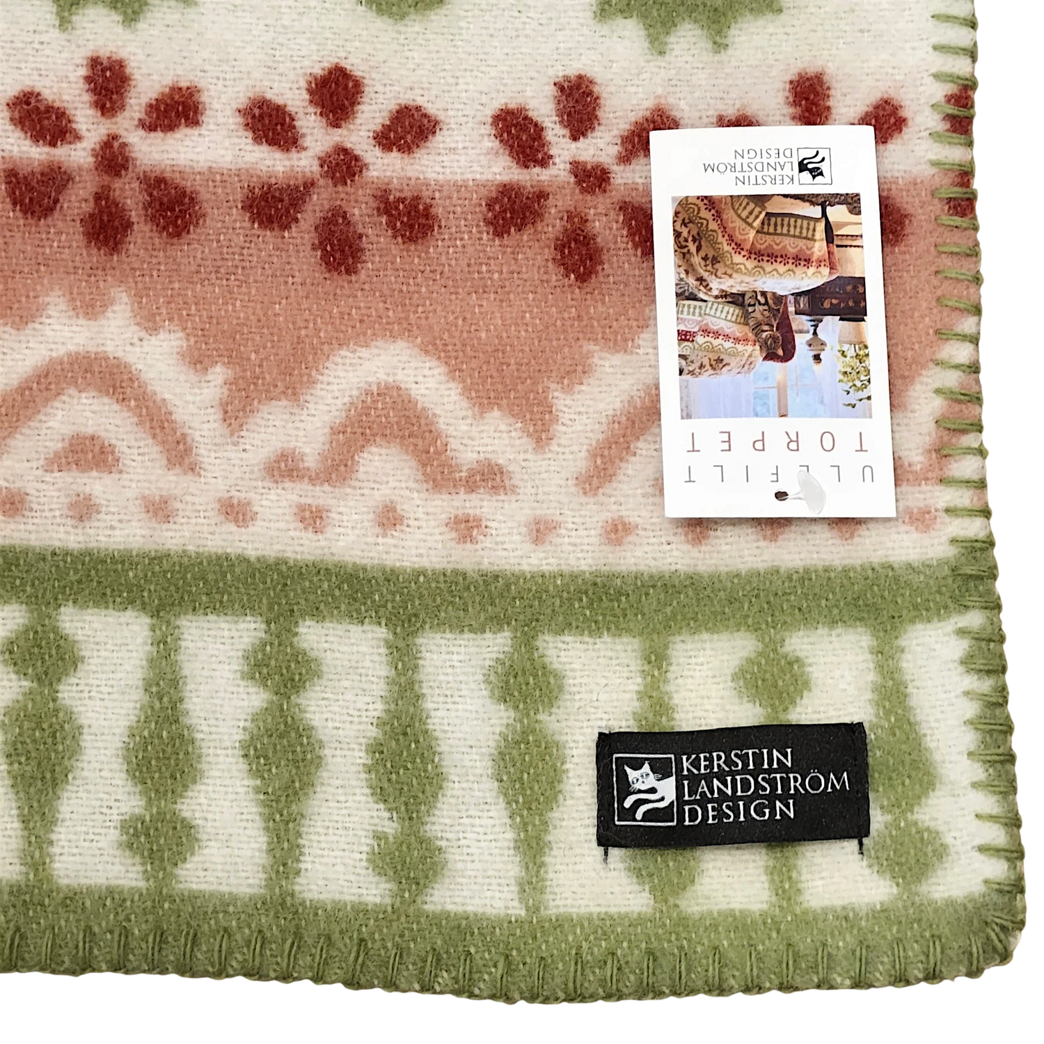 Swedish wool throw featuring green, red, and ivory patterns, with a product tag attached showing images of people wearing similar lambswool blankets.