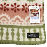 Swedish wool throw featuring green, red, and ivory patterns, with a product tag attached showing images of people wearing similar lambswool blankets.