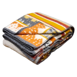 Folded Swedish blanket with a geometric pattern in yellow, orange, gray, and white, made from lamb’s wool and finished with contrasting stitched edges.