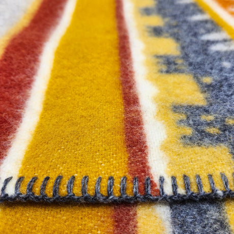 Close-up of a Swedish blanket with yellow, red, white, and blue geometric patterns and visible dark stitching along the edge.