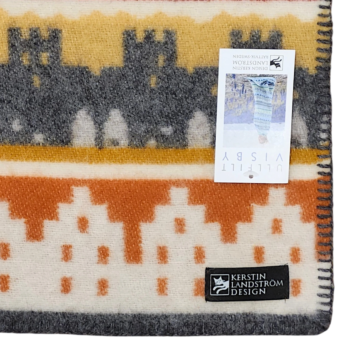 A Swedish blanket made from Norwegian lamb’s wool, featuring orange, yellow, and gray geometric patterns, a black Kerstin Landström Design label, and a product tag underneath.