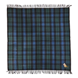 Square Black Watch tartan blanket featuring dark green and blue plaid pattern, fringed edges, and a small fabric tag sewn into one corner.