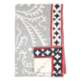 Folded gray fleece blanket with white leaf patterns and a red border featuring black diamond shapes, displayed on a plain white background.